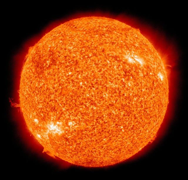 A close-up image of the sun. The sun is dark orange and has small light yellow spots that are solar flares.